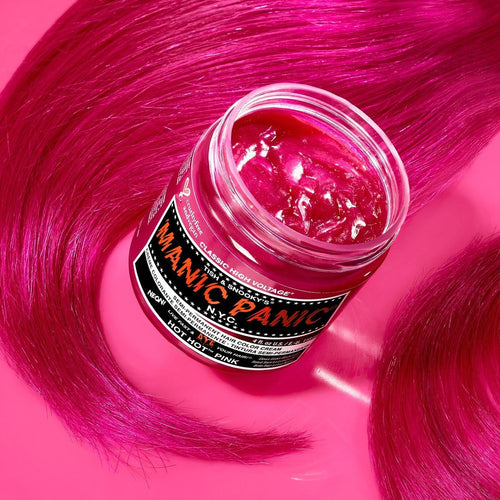 A jar of manic panic hair dye in hot hot pink color, surrounded by strands of vibrant pink hair splayed out on a vivid pink background.