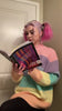 Woman with Pink hair sitting in the corner reading the book, Manic Panic: Living in color.