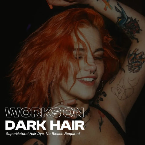 Smiling person with vibrant copper-orange hair dancing with arms raised, showing bold Manic Panic SuperNatural™ hair dye results on dark hair. Text overlay reads ‘Works on Dark Hair. SuperNatural Hair Dye. No Bleach Required.