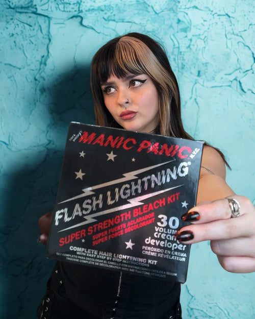 Person holding a Manic Panic Flash Lightning hair bleach kit against a textured blue wall.