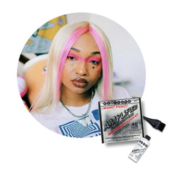 A circular inset shows a woman with long platinum-blonde hair featuring bright pink streaks, wearing makeup and jewelry, while the main image displays a Manic Panic Amplified Hair bleachr Kit bottle and applicatorbrush on a white background.
