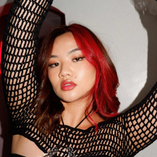 Person wearing a black fishnet top with red hair against a neutral background