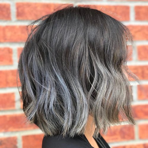 model with dark gray hair  in front of a brick wall